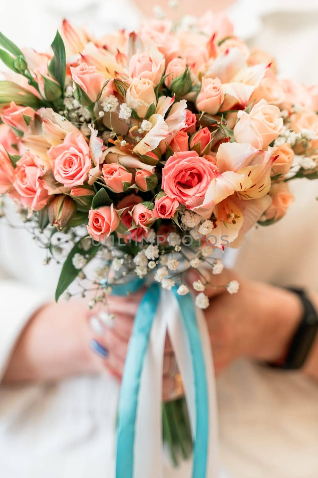 A woman is holding a bouquet of pink and white flowers. The woman is wearing a white shirt and a blue ribbon