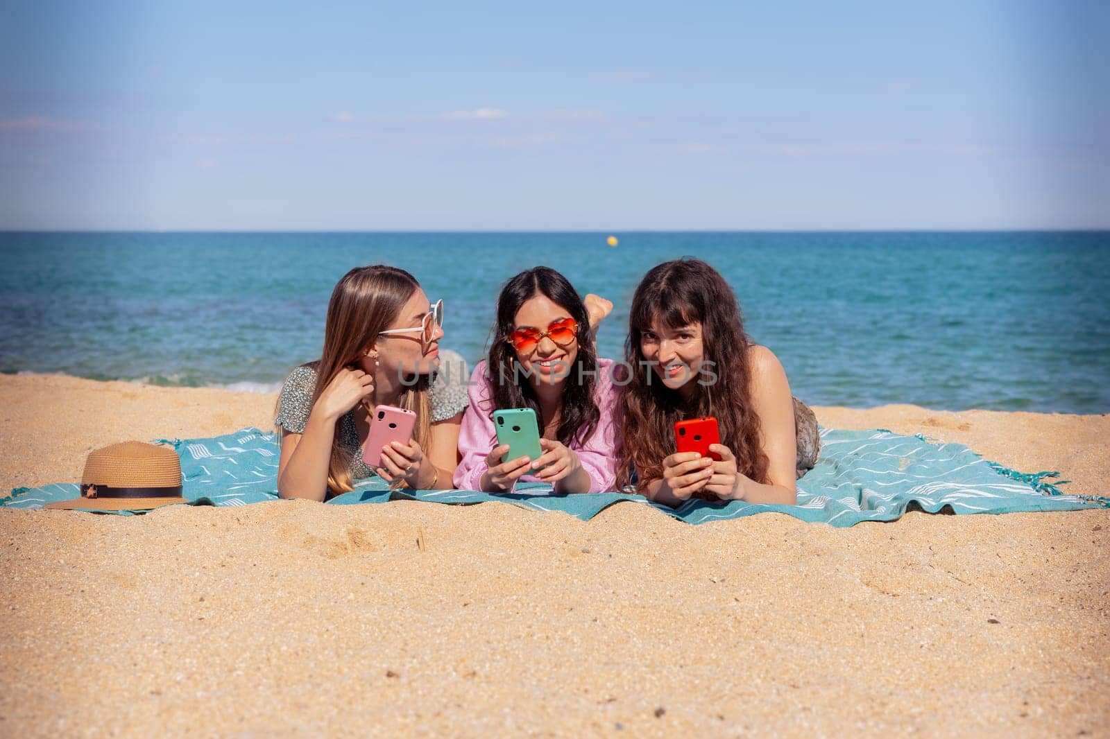 Group of smiling multiethnic women enjoying vacation. Beautiful and cheerful Gen Z girls with their mobile phones pose looking at the camera with a mobile phone.