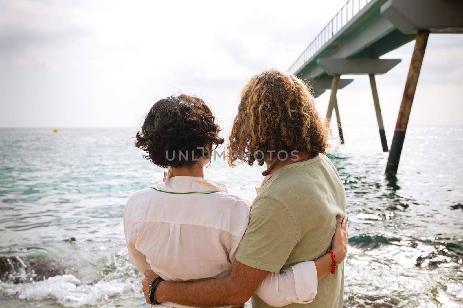 Rear view two happy friends sitting on the beach on vacation,looking at the sea. by molesjuny