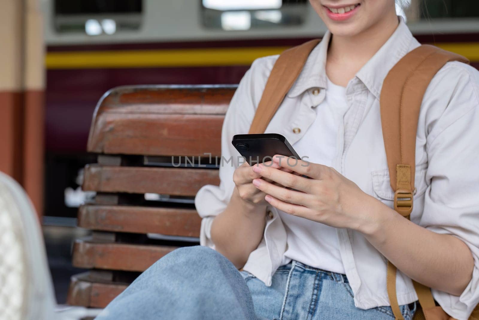 Young Woman Waiting for Train at Station, Using Smartphone, Casual Outfit, Backpack, Relaxed Atmosphere by wichayada