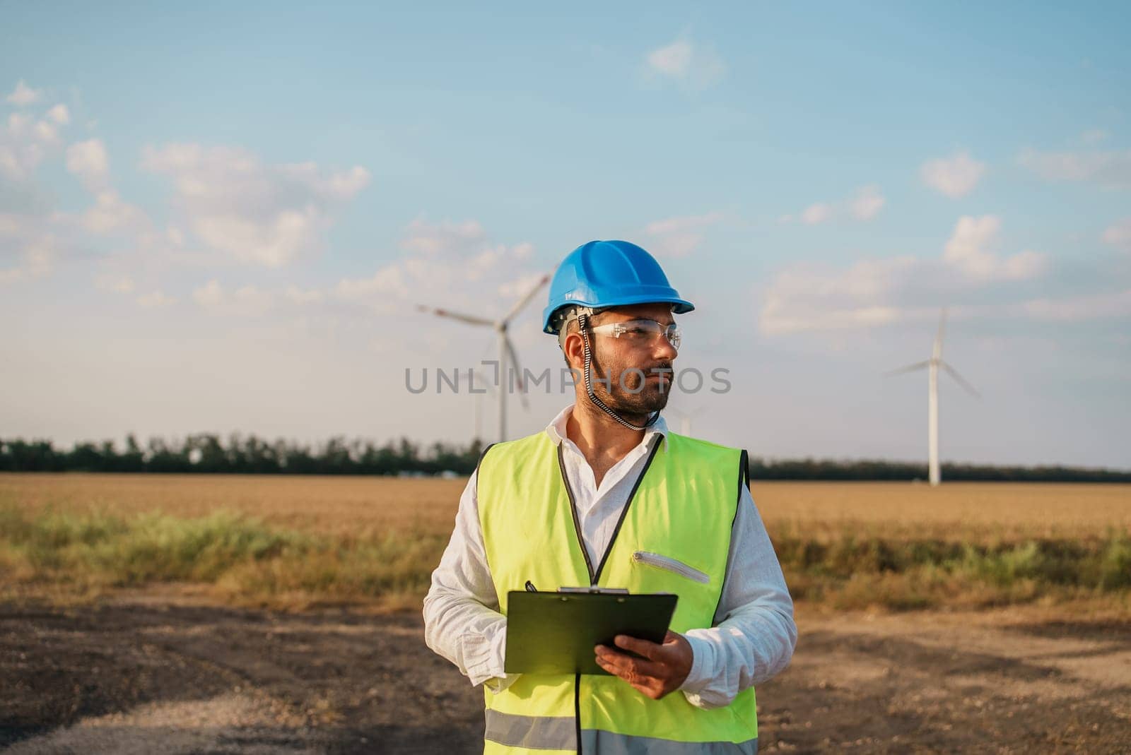 Maintenance engineer checking wind turbine farm on a field. Portrait of skilled professional. European green deal.