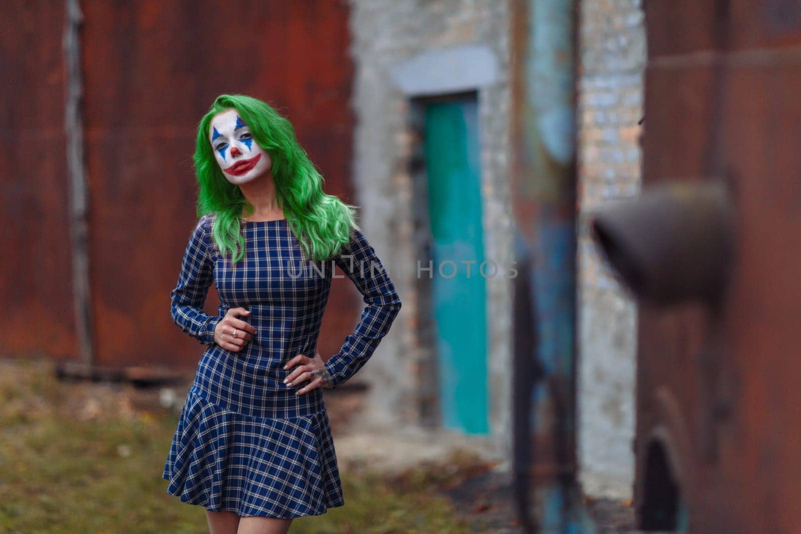 Portrait of a greenhaired girl in chekered dress with joker makeup on a atmospheric rusty metal wall background.