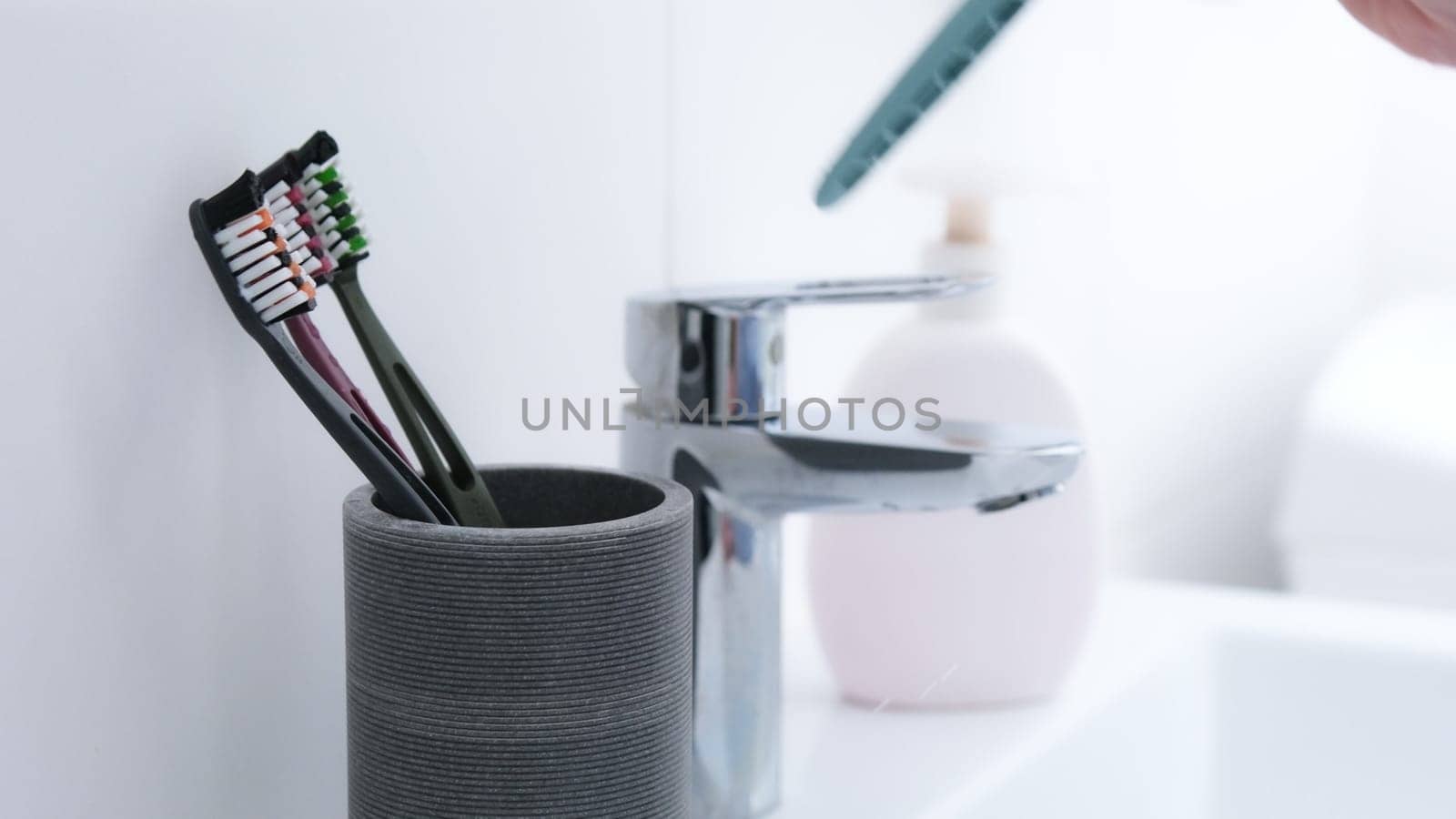 Woman'S Hand Throws Toothbrush Into Glass With 4 Toothbrushes Already In It