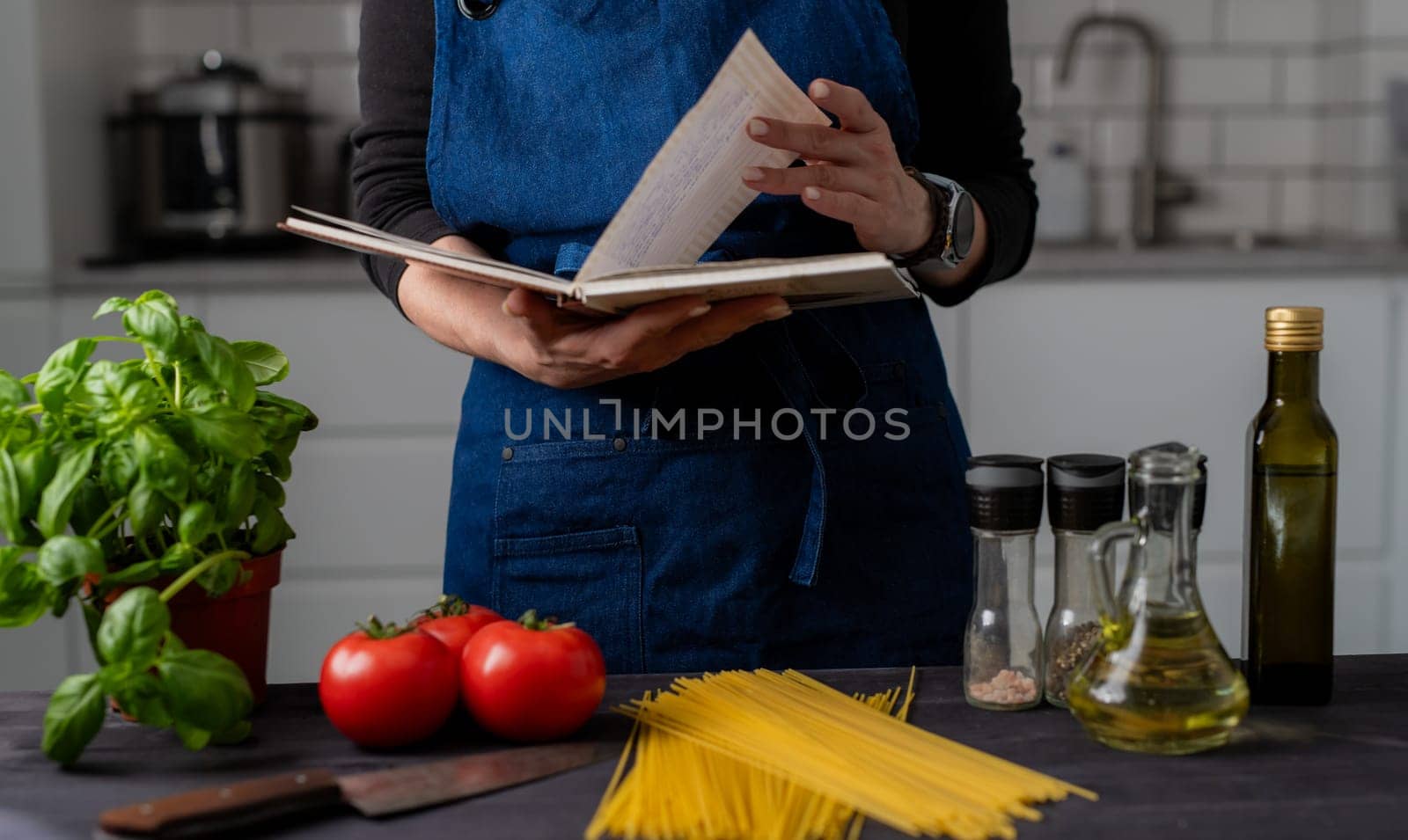 Woman Reads Recipe Near Table With Pasta, Tomatoes, Spices, And Basil