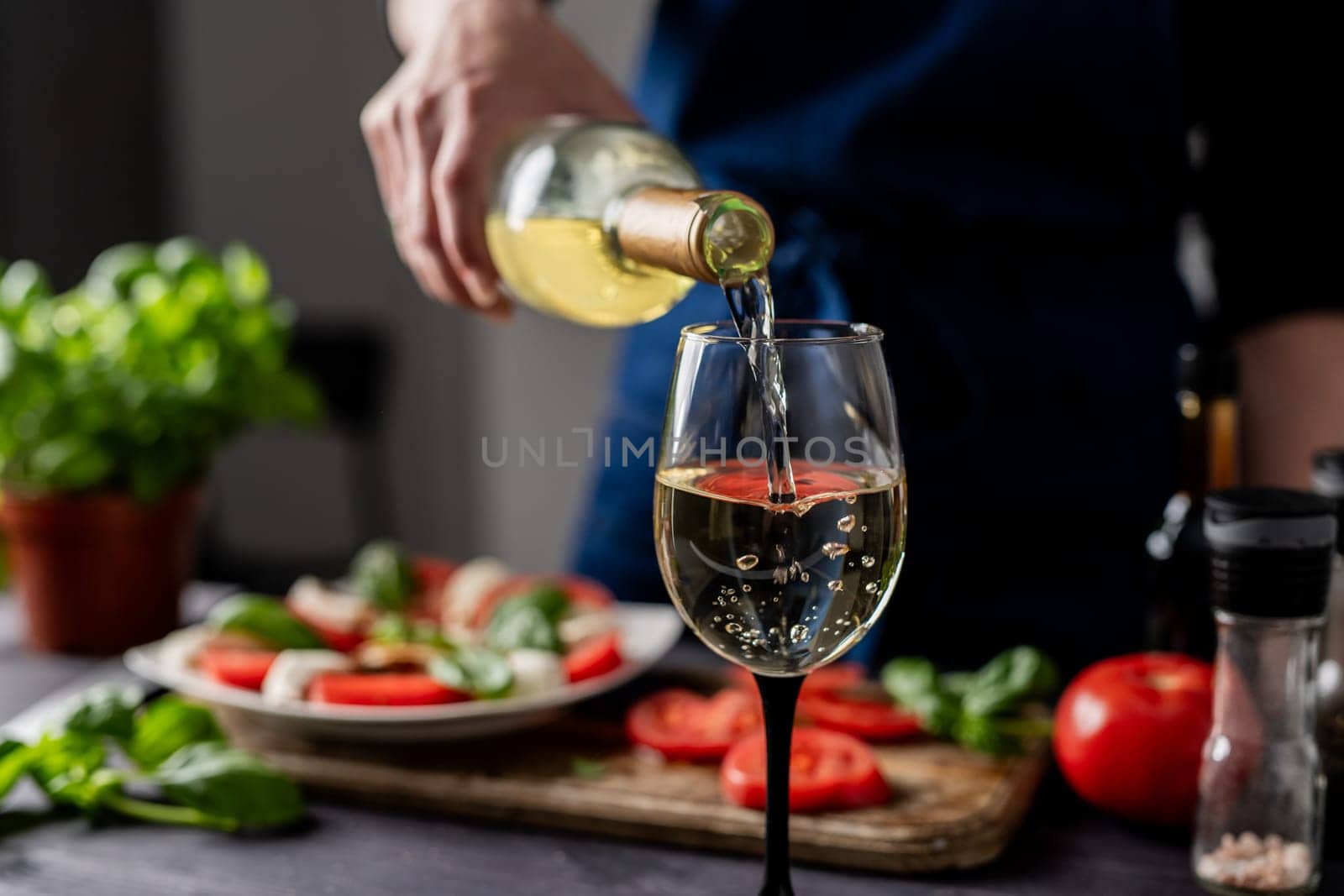 Woman'S Hand Pours Wine Into Glass Against Backdrop Of Caprese Salad, Close-Up View
