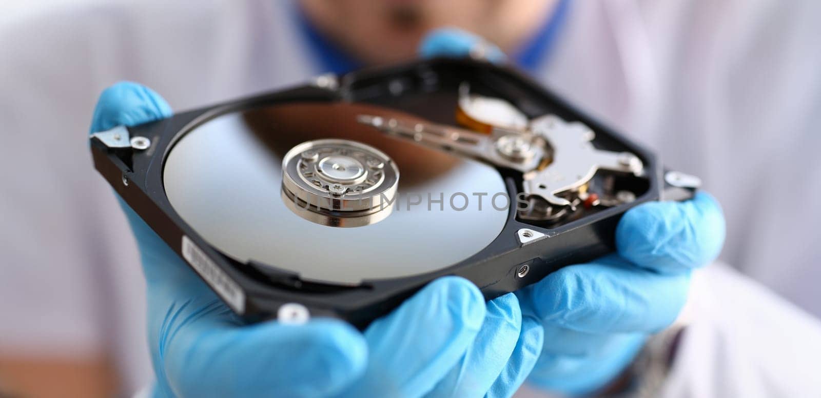 A male repairman wearing blue gloves is holding a hard drive from computer or laptop in hands. Performs fault diagnostics and performs urgent repairs recovery of lost data during deletion HDD closeup