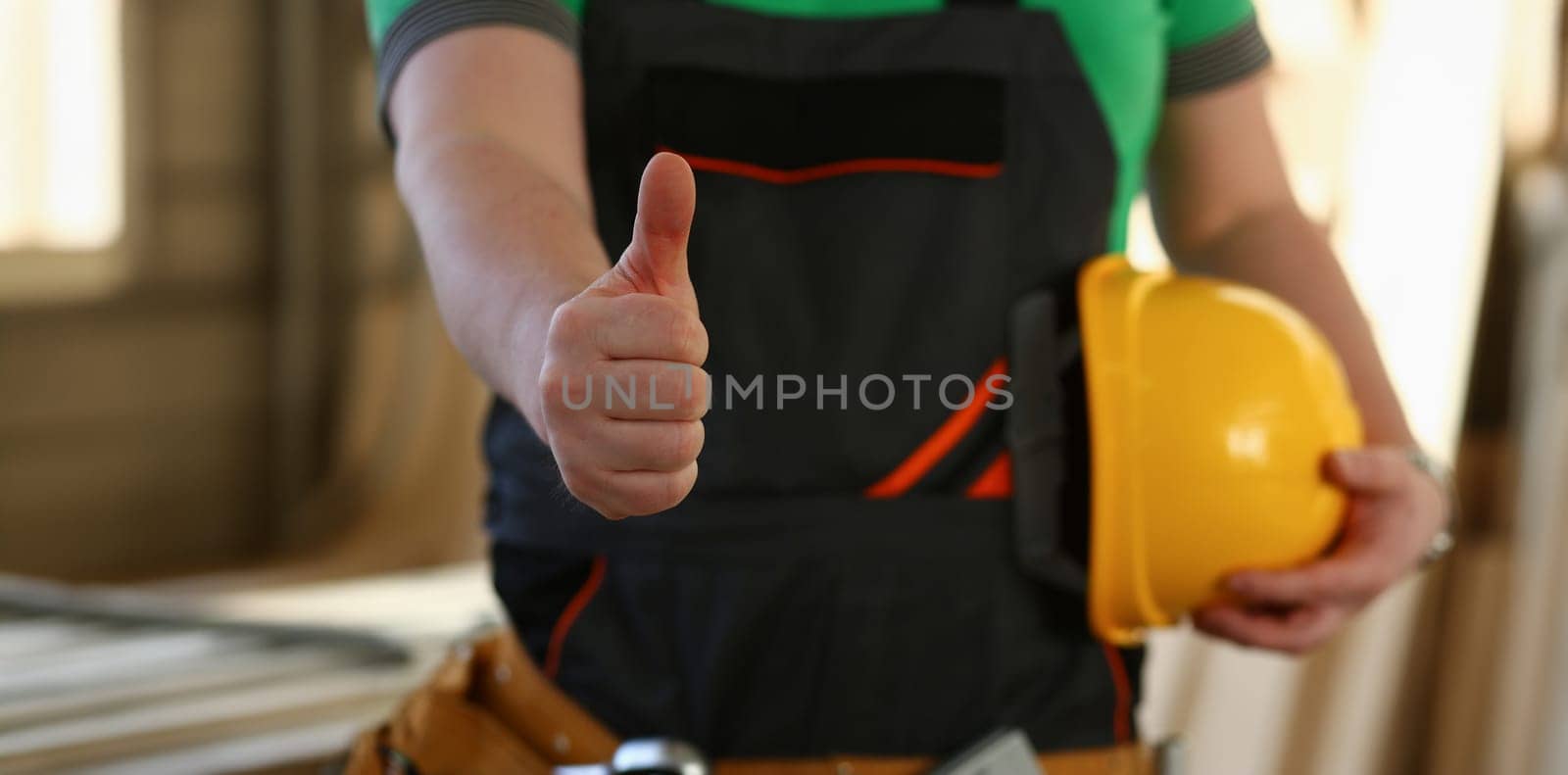 Hand of worker in yellow helmet show confirm sign with thumb up at arm portrait. Manual job DIY inspiration joinery startup idea fix shop hard hat industrial education profession career concept