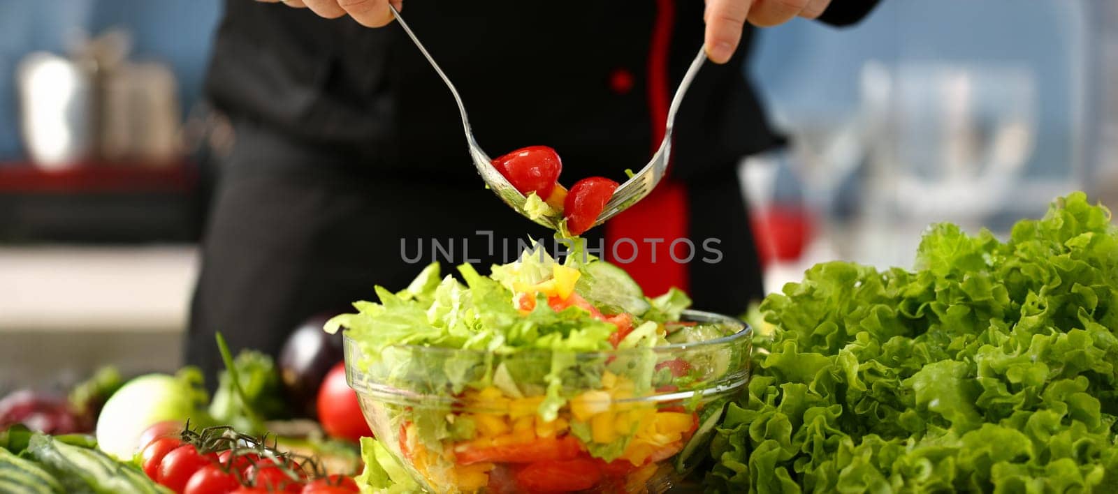 Cook holds fork in hand and mixes salad fresh vegetables seasoned with olive oil. Raw food and vegetarian in modern society is popular concept.