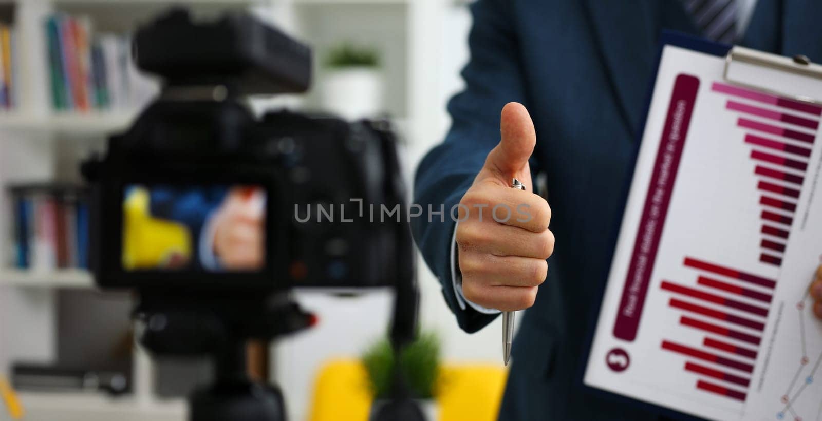 Male in suit and tie show confirm sign arm making promo videoblog or photo session in office camcorder to tripod closeup. Vlogger promotion selfie solution or finance advisor management information