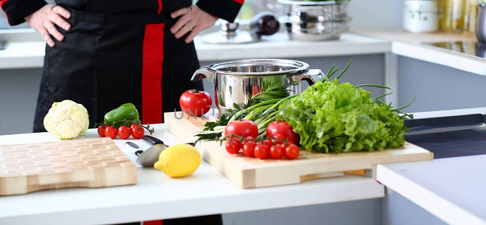 The cook in the kitchen is preparing to prepare a dish of fresh vegetables for a vegan, keeps his hands on his belt, the products lie on the table