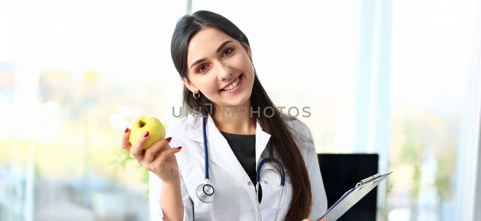 Young smiling woman doctor holds apple in hand portrait. Nutritionist talks about concept of healthy diet lifestyle for losing excess weight about benefits and harms vegetarianism.