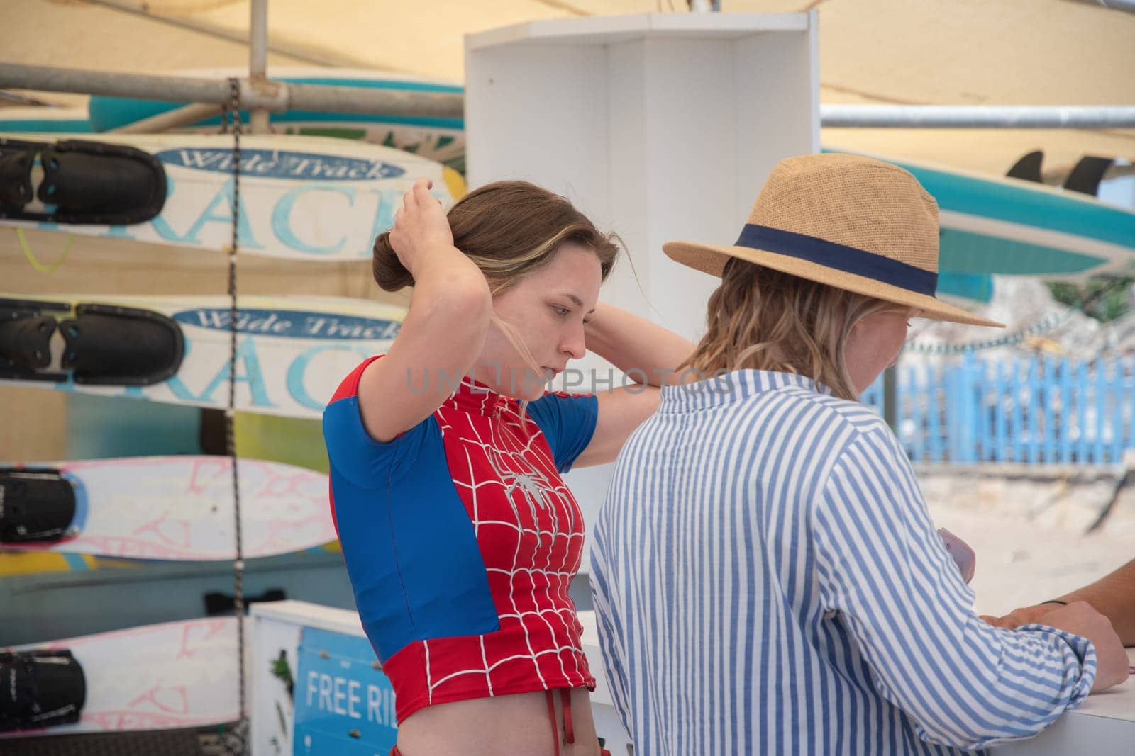 Teenage girl in swimsuit with Spiderman print and her mother choose water activities from the manager rental of water sports equipment, entertainment on the beach, Belek, Turkey, May 30, 2024