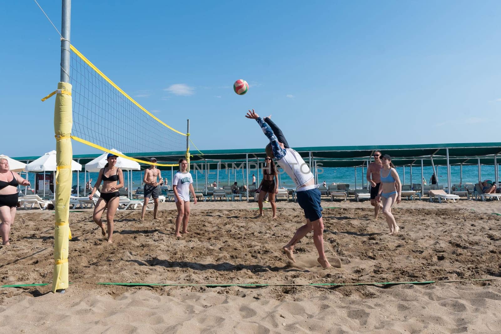 two teams of vacationers play beach volleyball at sea on vacation, the ball flies through the net against a clear blue sky, ball matches and active activities, Belek, Turkey, May 31, 2024