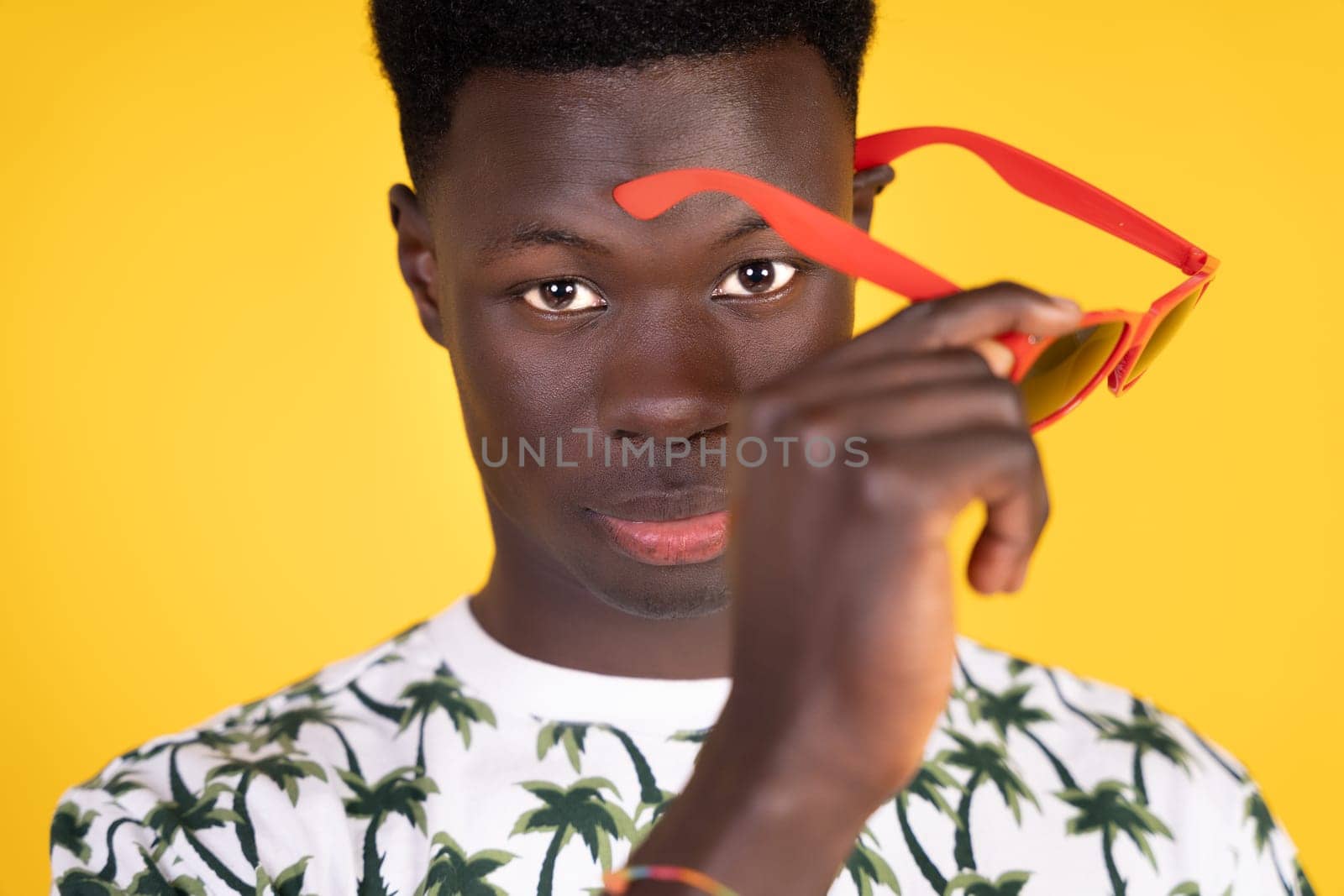 A man with a red pair of sunglasses is holding them up to his face by Ceballos