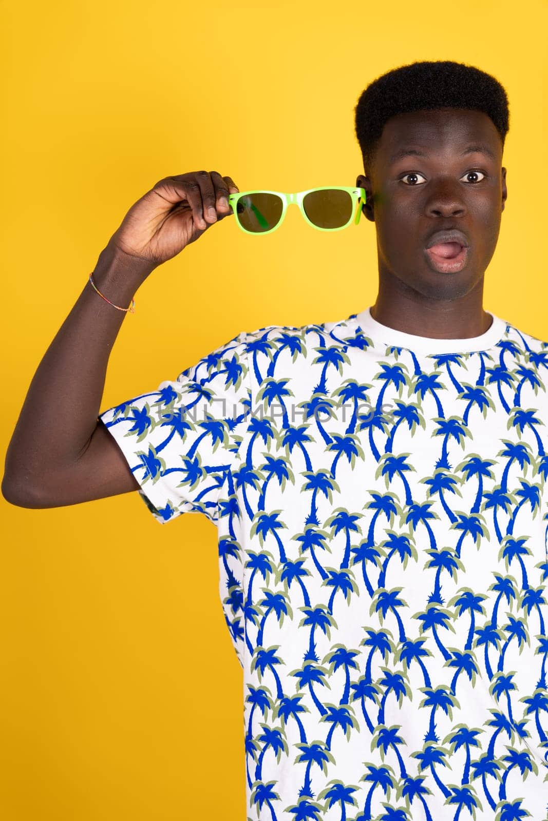 A man wearing a blue and white shirt with palm trees on it is holding sunglasses in his hand