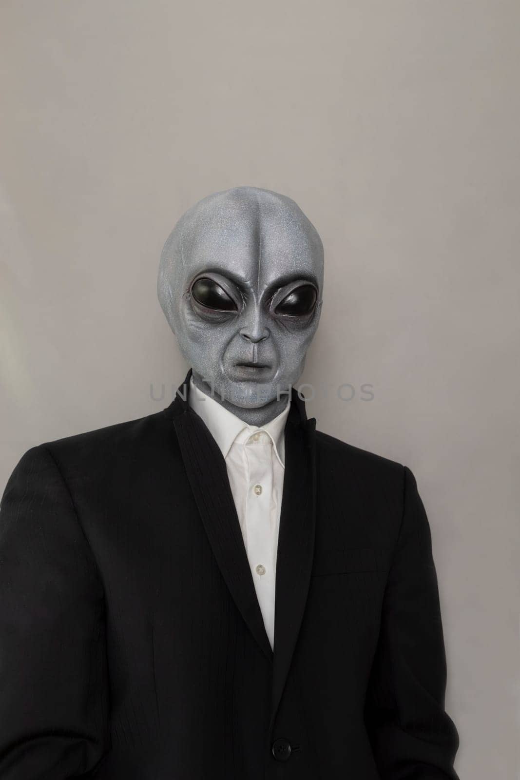 Portrait Of Alien Wearing Suit Gray Background. World UFO Day. Extra Terrestrial Being, Unidentified Flying Objects. Vertical Plane. Grey Humanoid. High quality photo