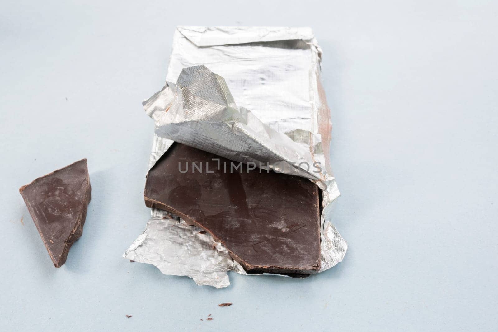 Opened chocolate, with unpacked foil, chipped pieces of chocolate on a blue background.