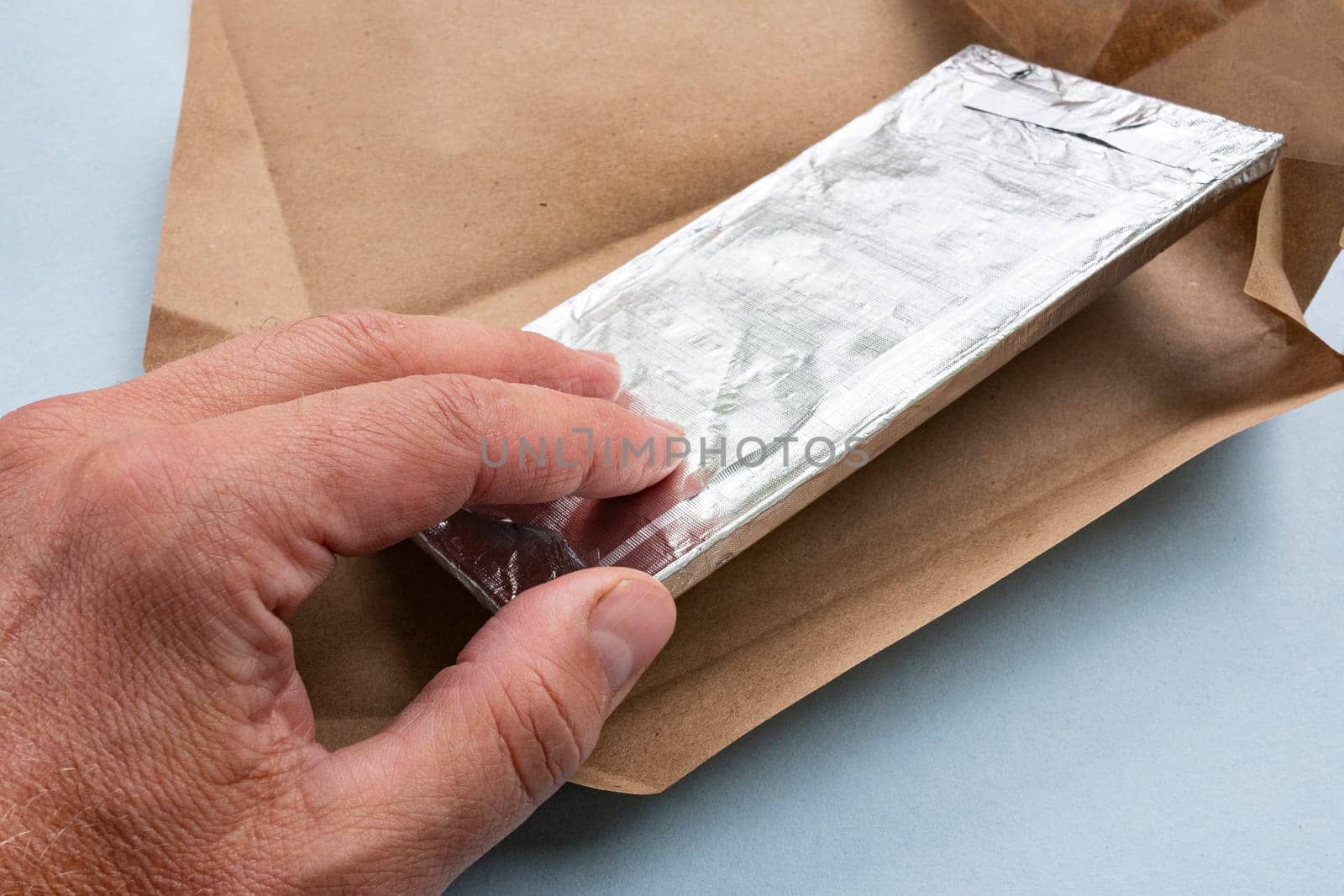 A man's hand unpacks chocolate and opens the paper packaging.