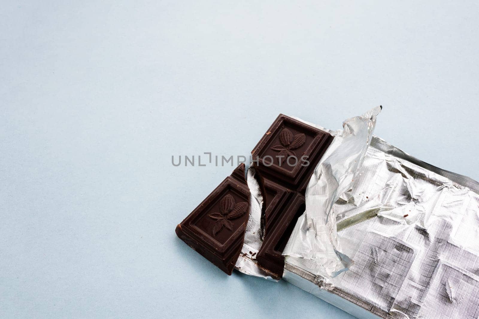 Opened chocolate with unpacked foil, cracked chocolate, broken piece of chocolate bar.