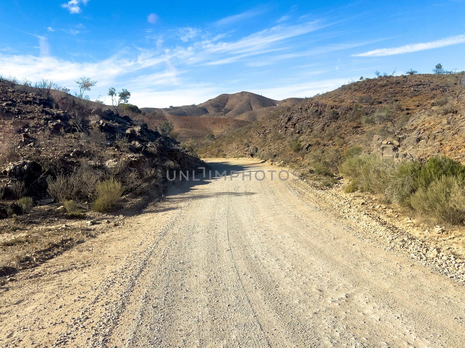 Winding dirt road through rugged terrain in Flinders Ranges under a clear blue sky.