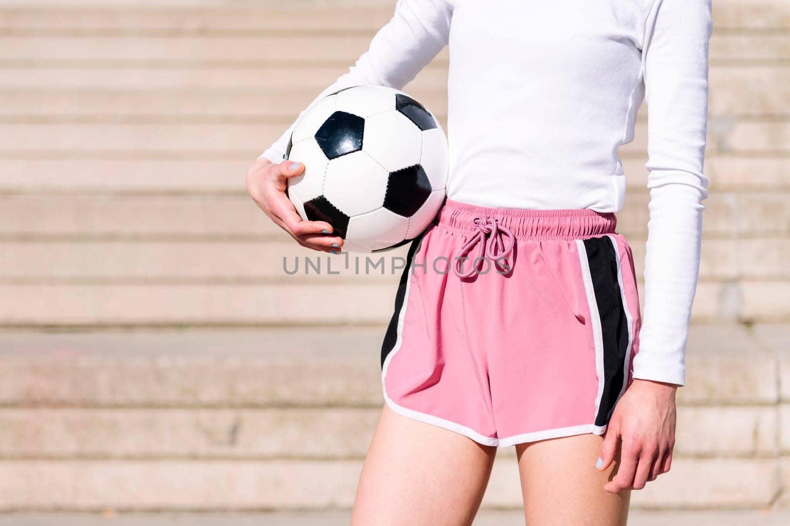 close up of an unrecognizable sports woman in a concrete soccer court with a ball under her arm, concept of football lifestyle and urban sport in the city, copy space for text