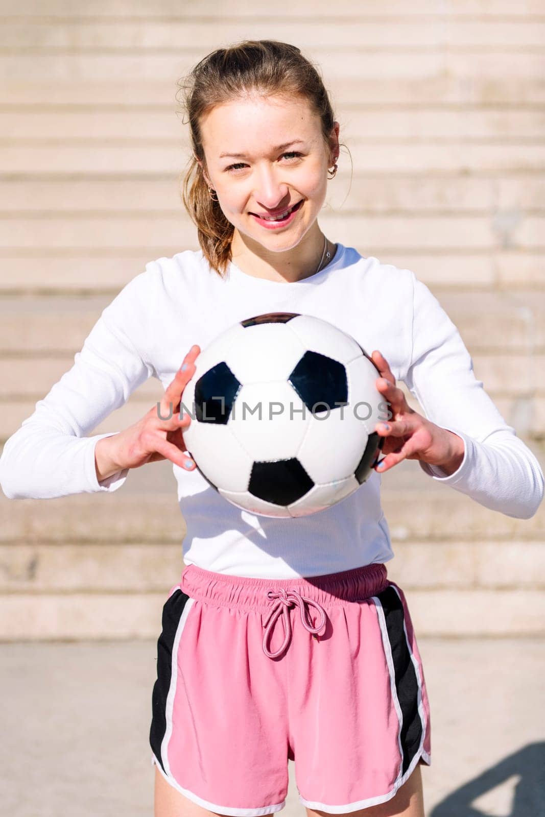 portrait of a smiling sports woman in a concrete soccer court with football ball in her hands, concept of football lifestyle and urban sport in the city