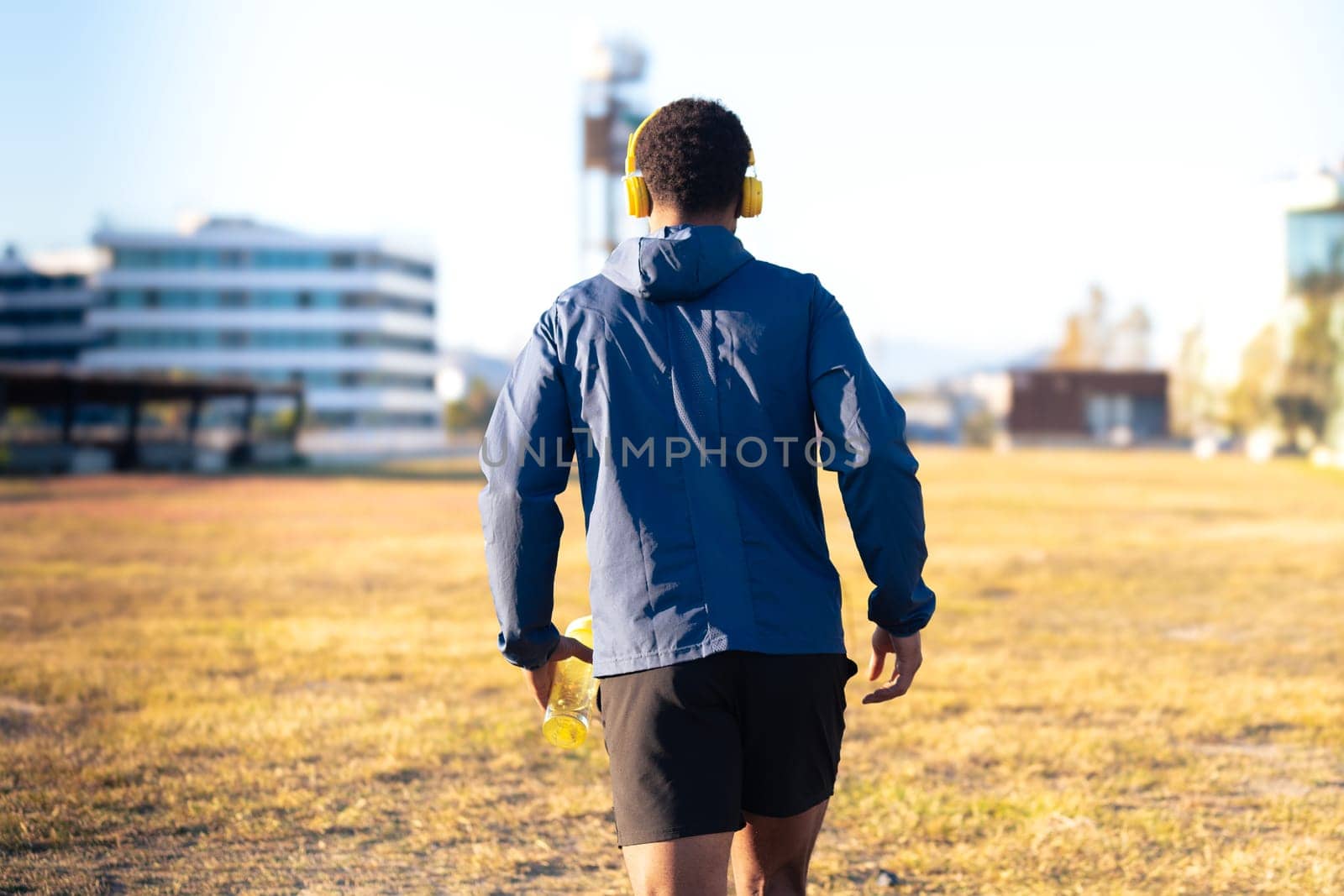 Rear view young man ready to run through the city streets, with a bottle of water outdoors by mariaphoto3