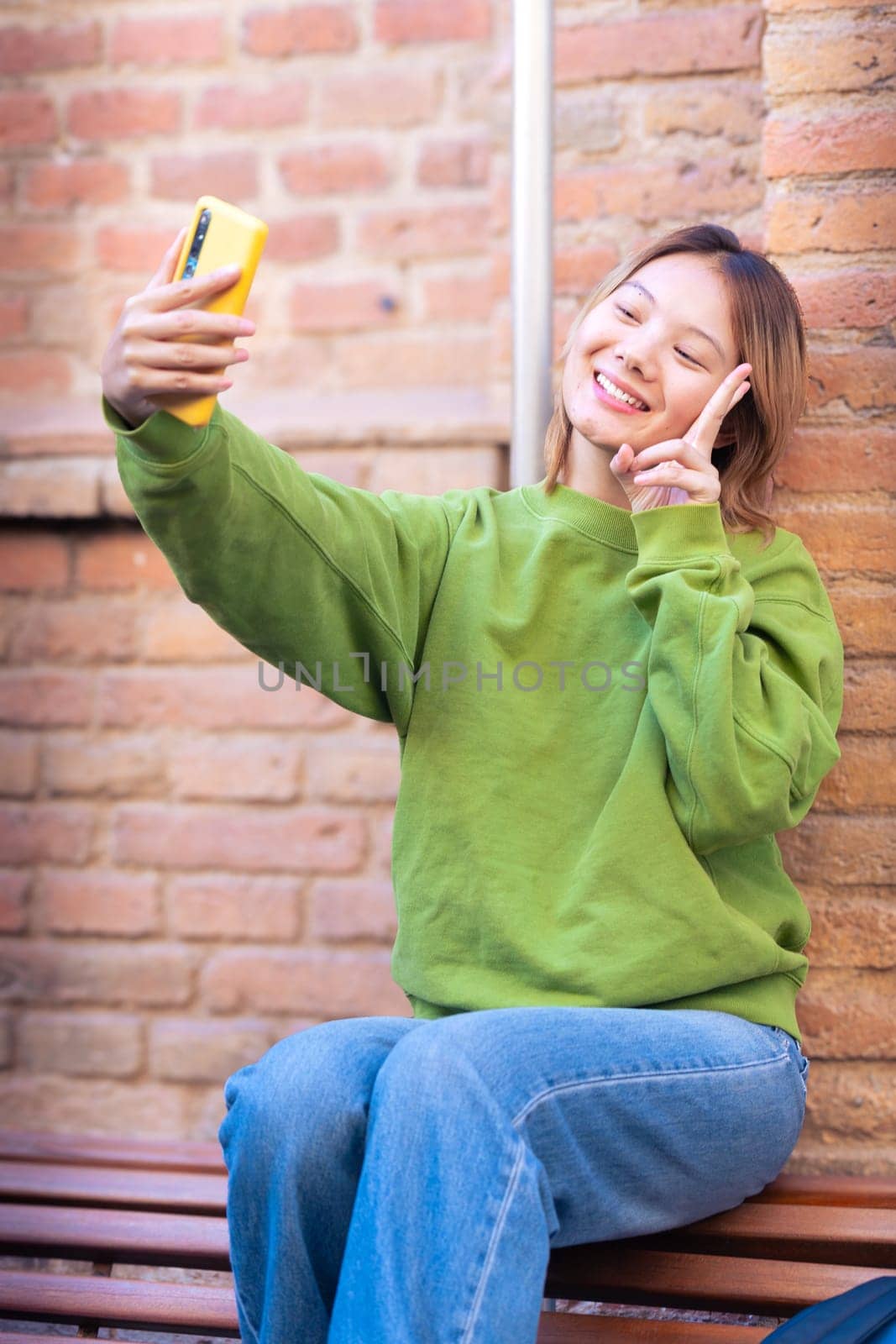 Young Asian woman having a video call with cell phone and smiling outdoors. by mariaphoto3