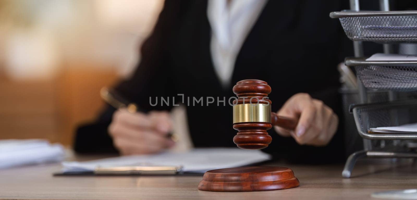 A female lawyer examines contract documents related to a lawsuit in an office setting, with a gavel prominently placed on the desk.