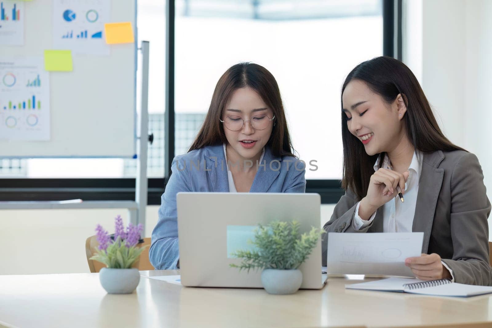 Two Female Accountant Collaborating on Financial Graphs and Data Analysis in a Modern Office Setting by wichayada