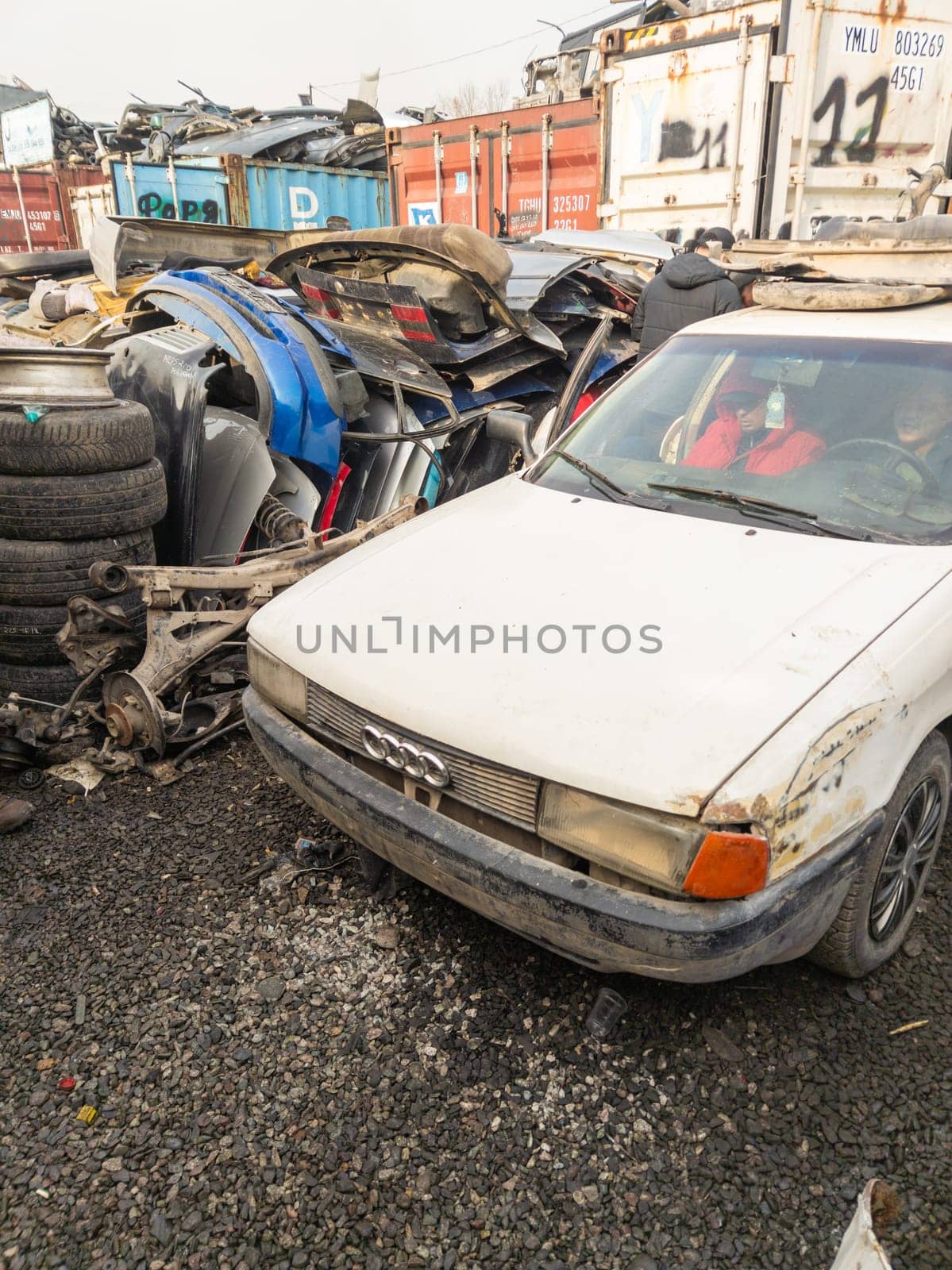 two sellers hiding from rain inside junk Audi car in a junkyard used car parts Kudaibergen market in Bishkek, Kyrgyzstan - November 11, 2022