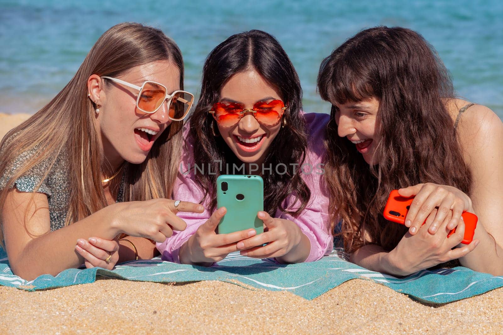 Group of smiling multiethnic women enjoying vacation. Beautiful and cheerful Gen Z girls with their mobile phones pose looking at the camera with a mobile phone.