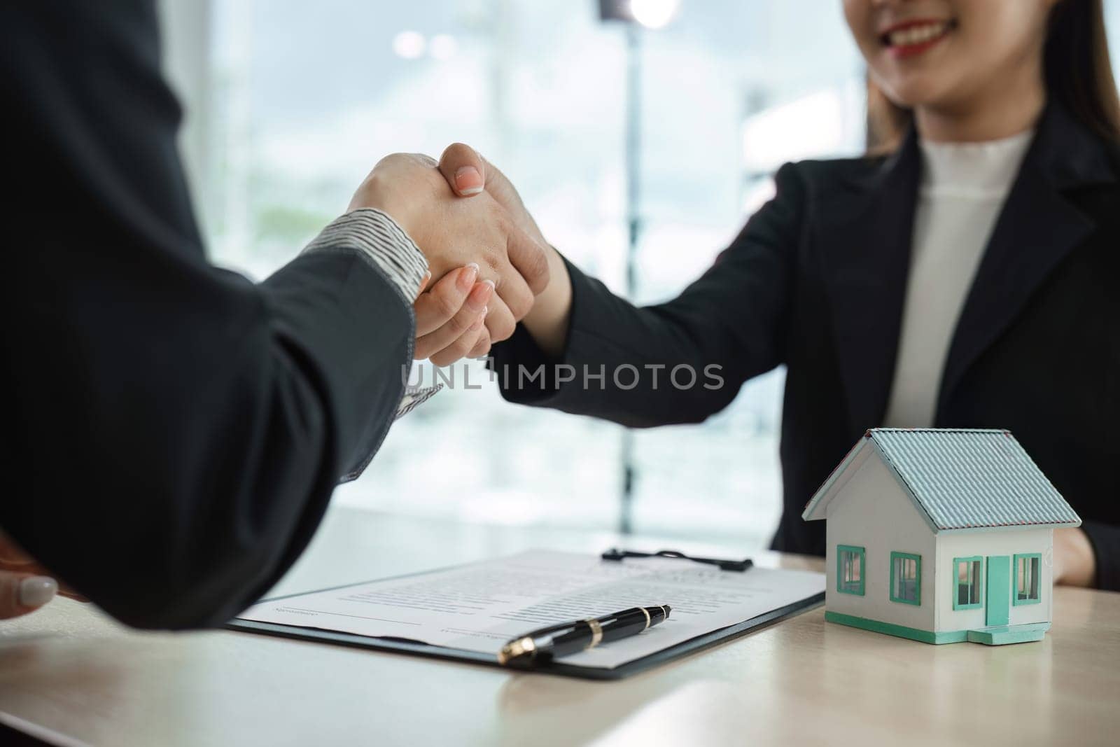 Real estate agent and client shaking hands over a house purchase agreement, symbolizing a successful deal in a modern office.