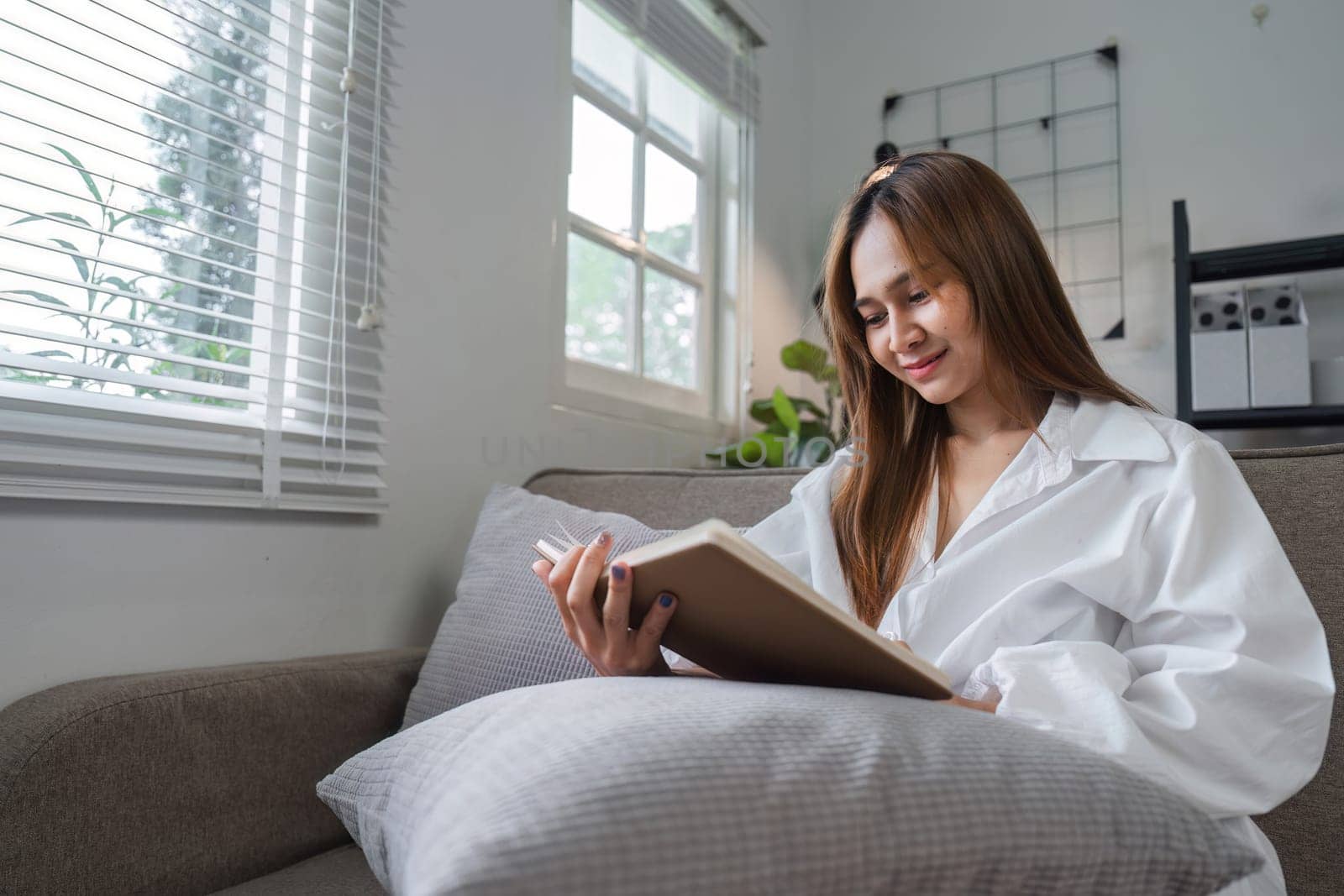 A woman sits comfortably on a couch, reading a book in the morning light, creating a serene and cozy atmosphere.