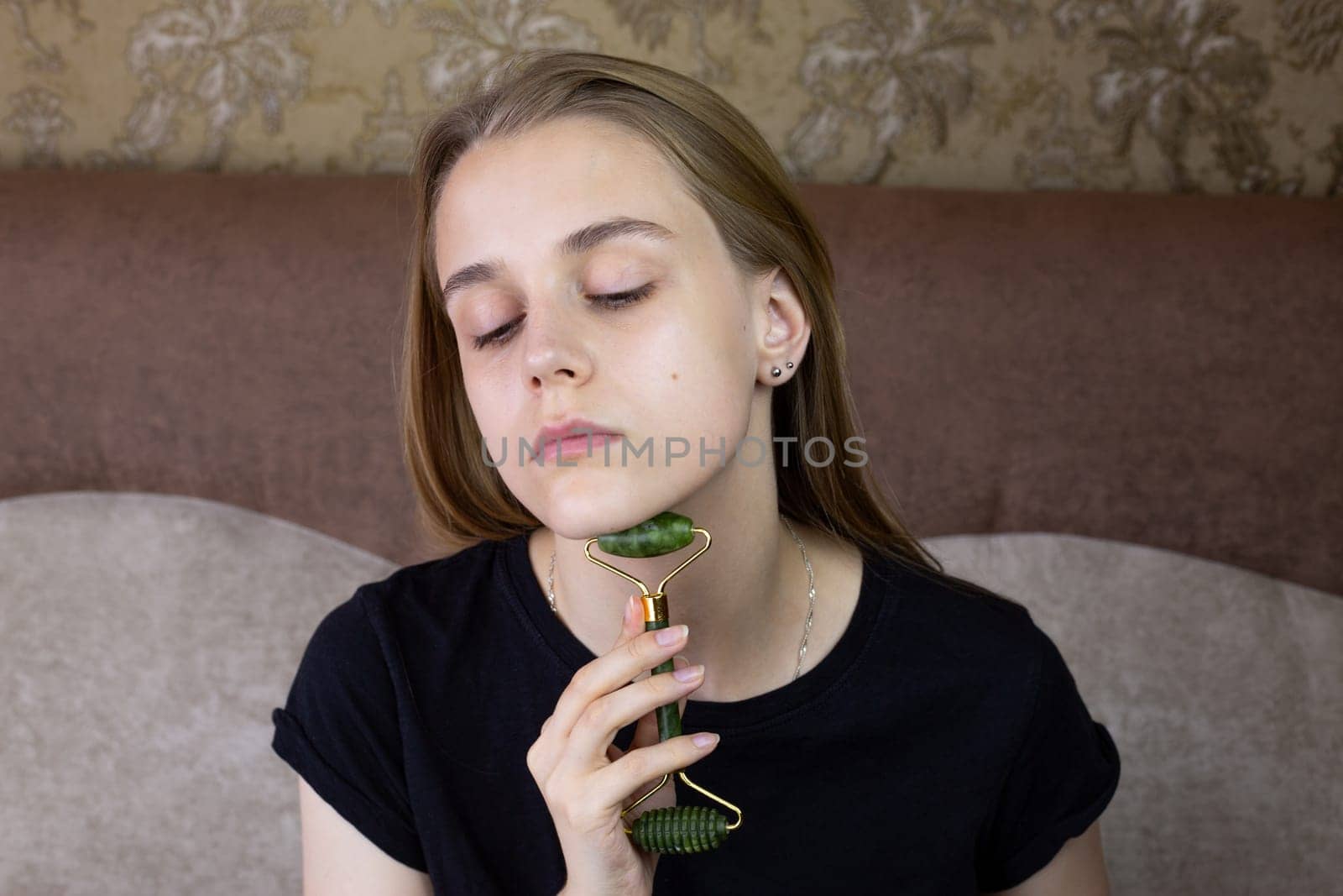 Young girl does chin massage with special jade stone roller to smooth out wrinkles on the skin, caring and freshening the skin of beautiful girl face