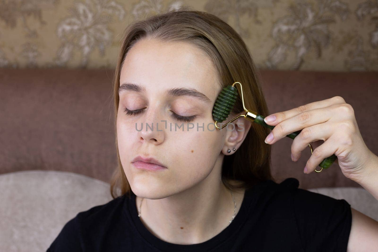 Young European girl makes facial massage using stone roller to smooth out wrinkles and take care of body skin for beauty