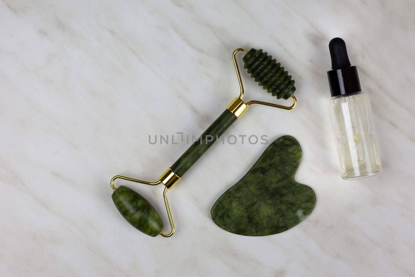 Facial massage and skin care set with special gua sha scraper, moisturizing oil and wrinkle smoothing stone roller lies on white table