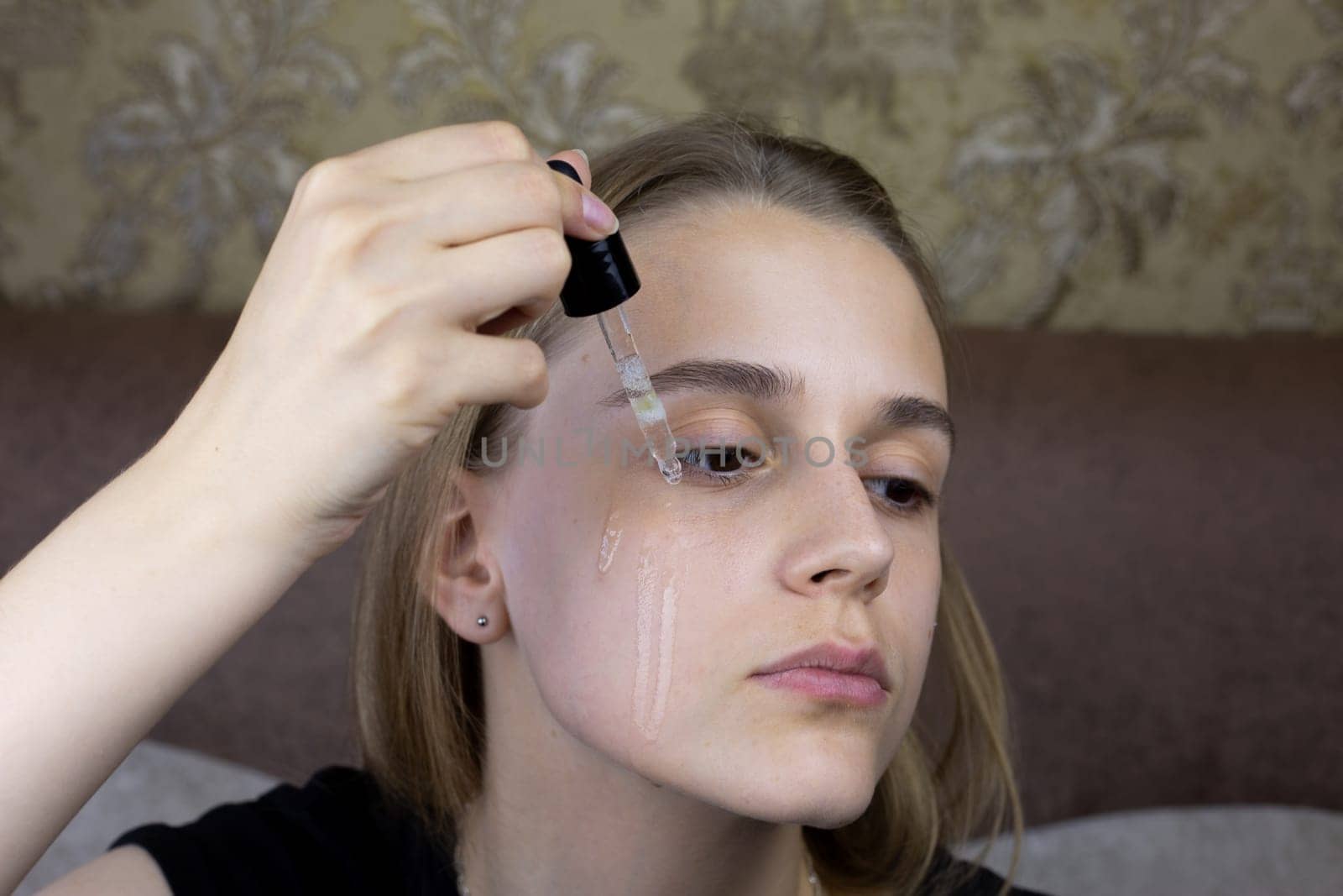 European girl is dripping special massage oil for skin care onto her face, pipette with dosage of product for healthy facial skin