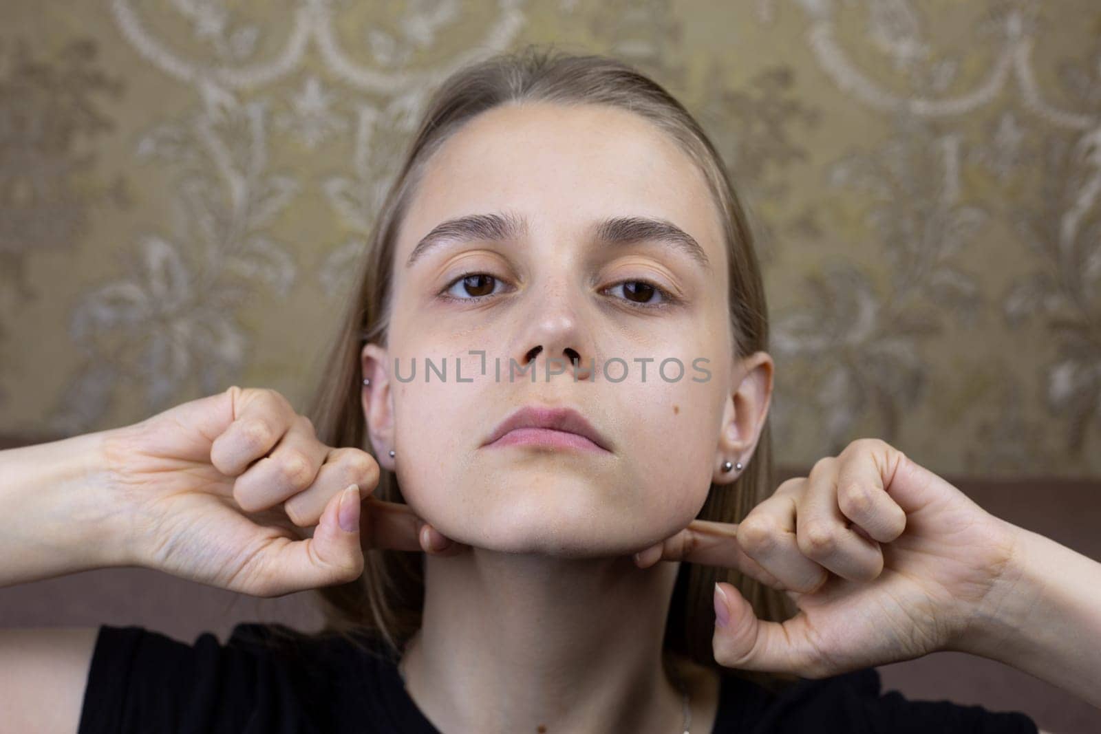 Young girl smooths out wrinkles on her face with hands with special oil for massage, beauty procedure of European girl for body skin care