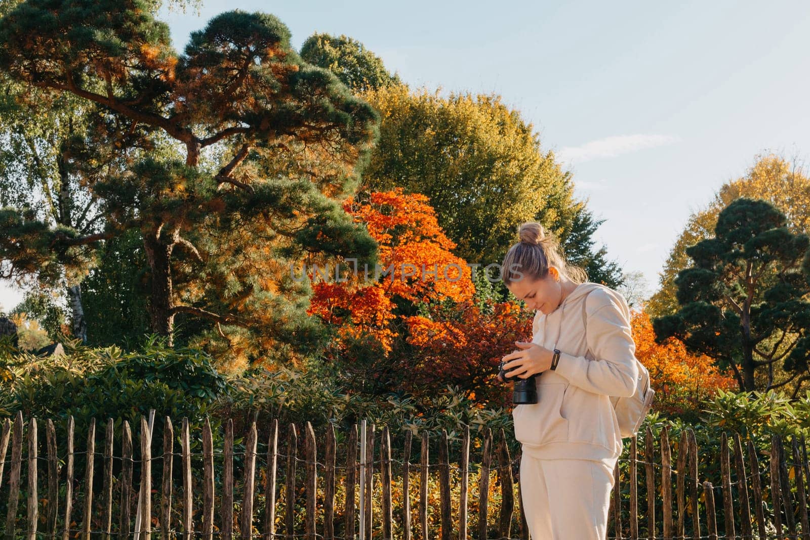 Beautiful young woman takes photos with a professional camera in autumn forest. Smiling girl enjoying autumn weather. Rest, relaxation, lifestyle concept. Young photographer takes pictures of autumn forest at sunset by Andrii_Ko