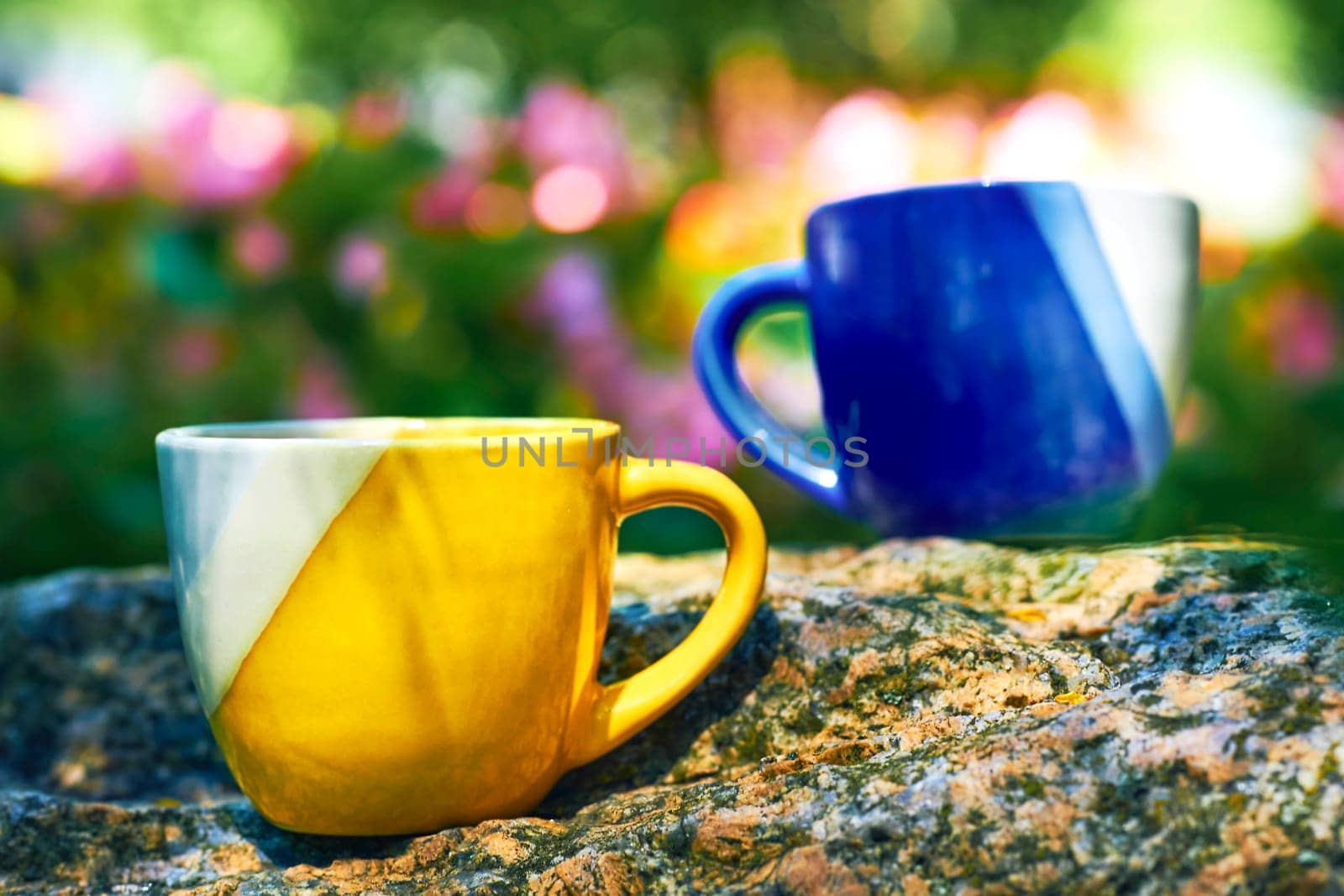 Coffee break,tea time.Yellow blue cups on stone in flower garden by jovani68