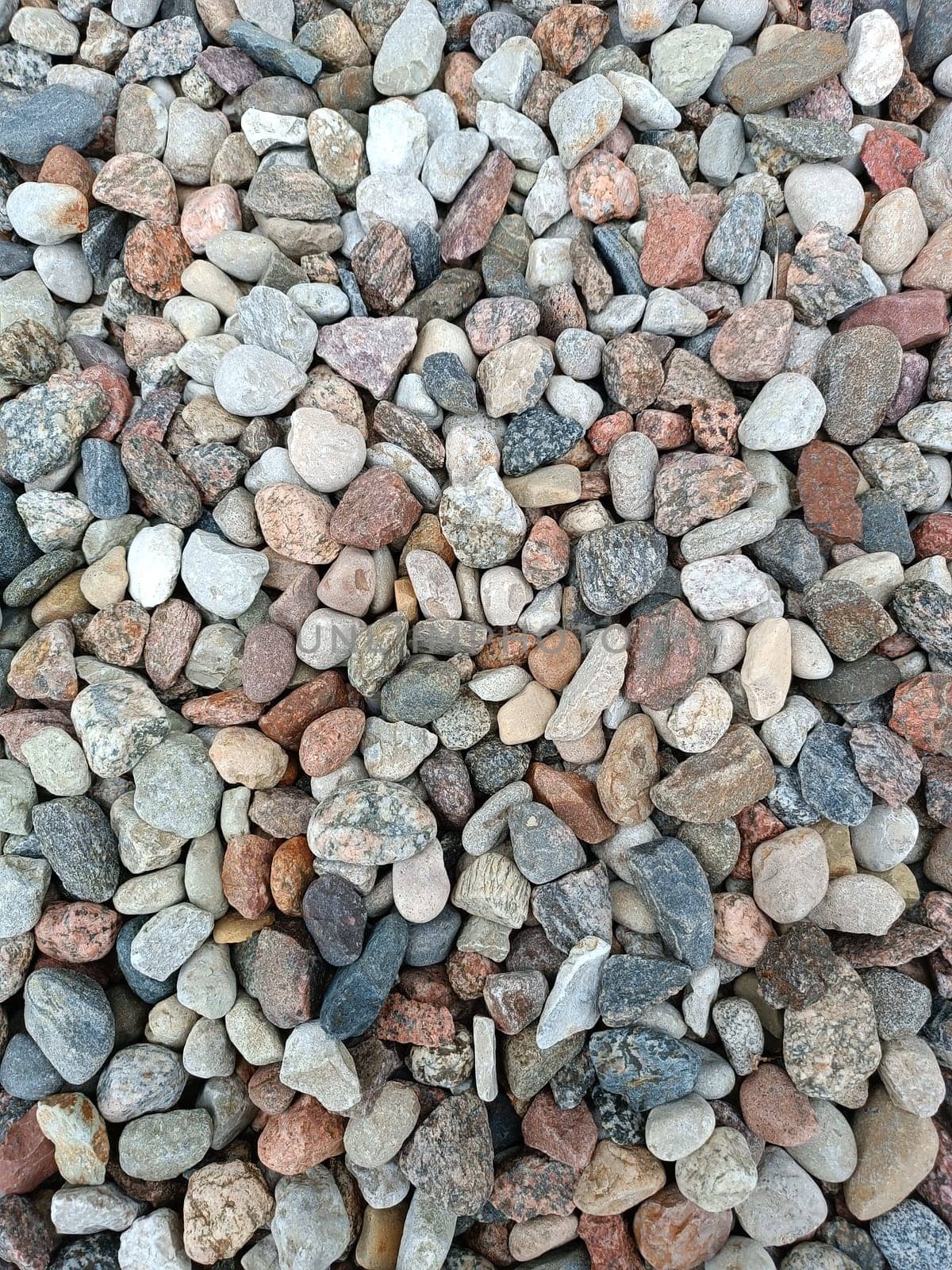 Stone beach background. Coastline pebbles beach. Stones on beach. Decorative texture of stones. Coloured stone on coastline. Stone background, texture. High quality photo. Mobile vertical photo