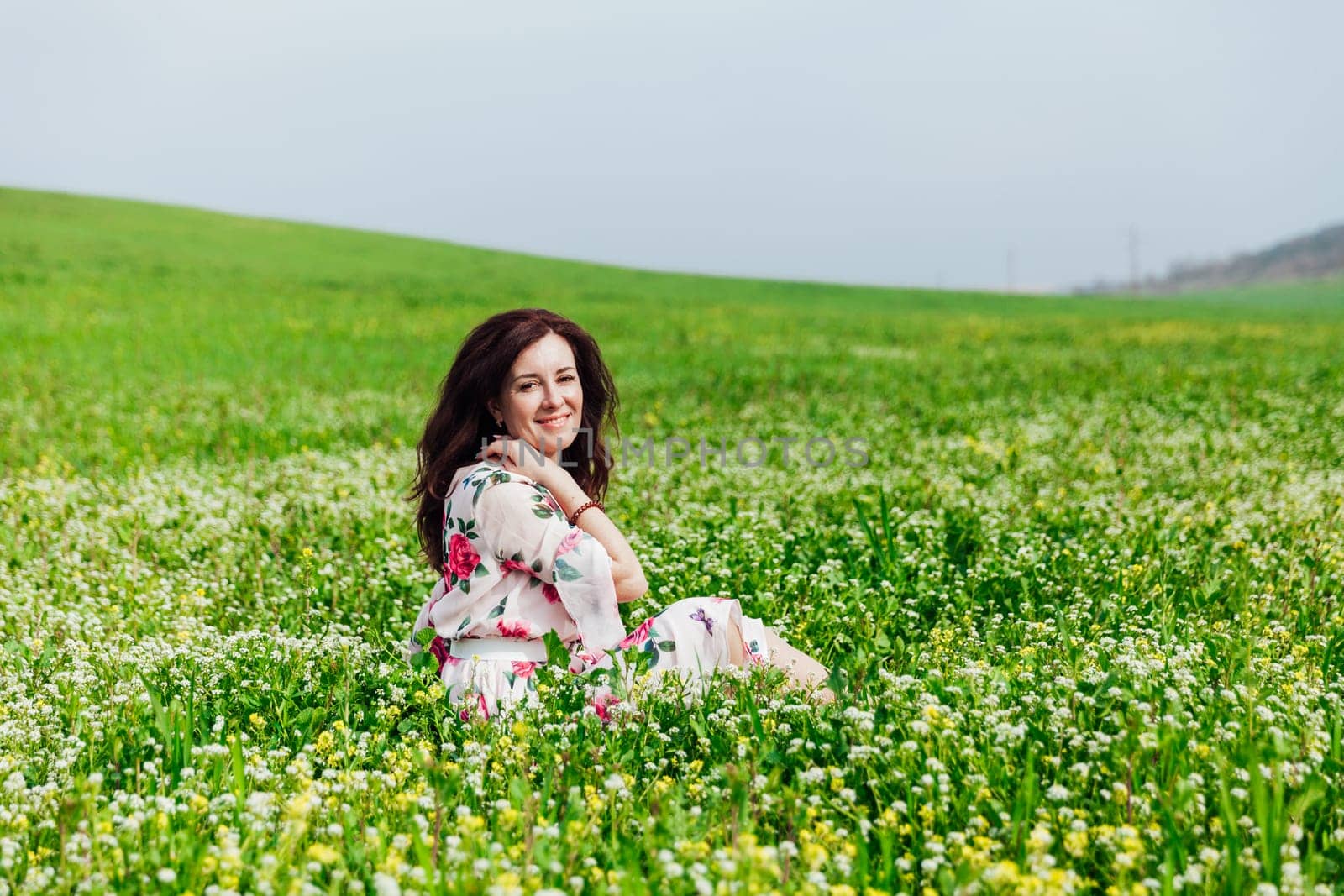 a beautiful brunette sits in white flowers in a green clearing in a park in nature