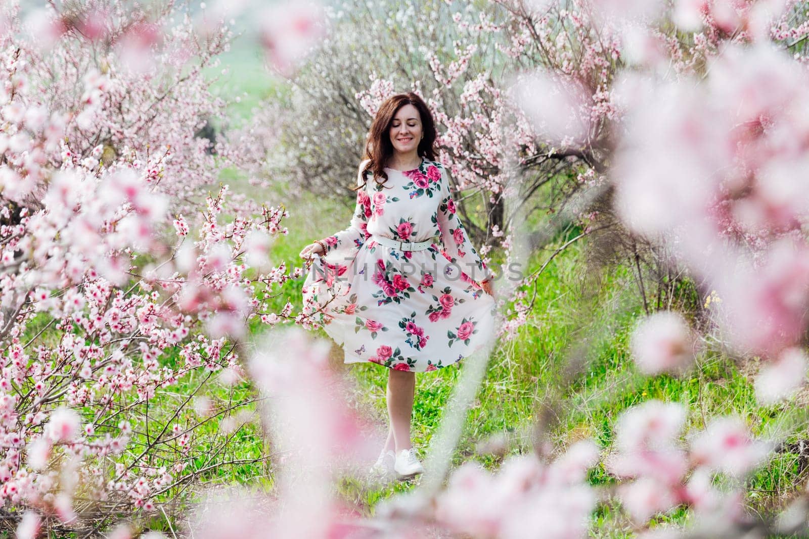 brunette in beautiful dress in pink flowers in a blooming garden walk in spring