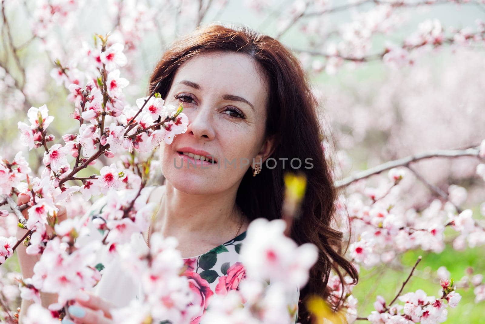 portrait of beautiful brunette woman in pink flowers on the street in a blooming garden