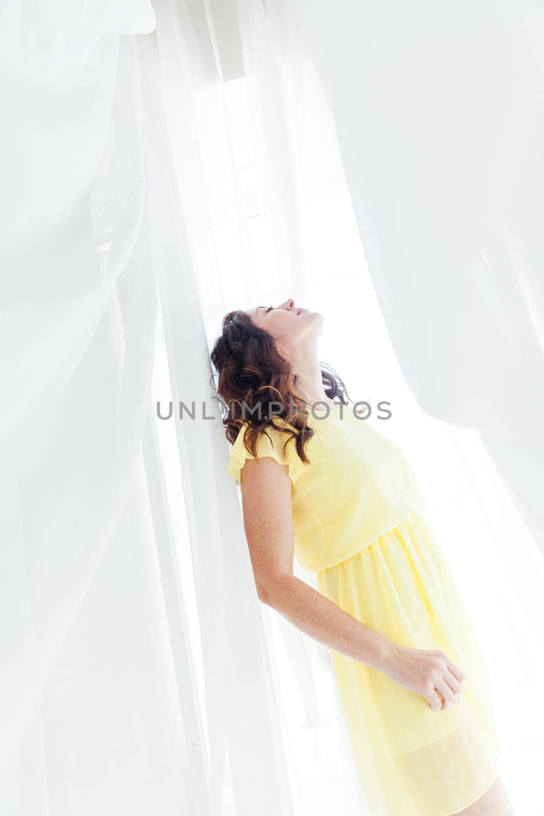 woman in a yellow dress looks up in white fabrics in the room