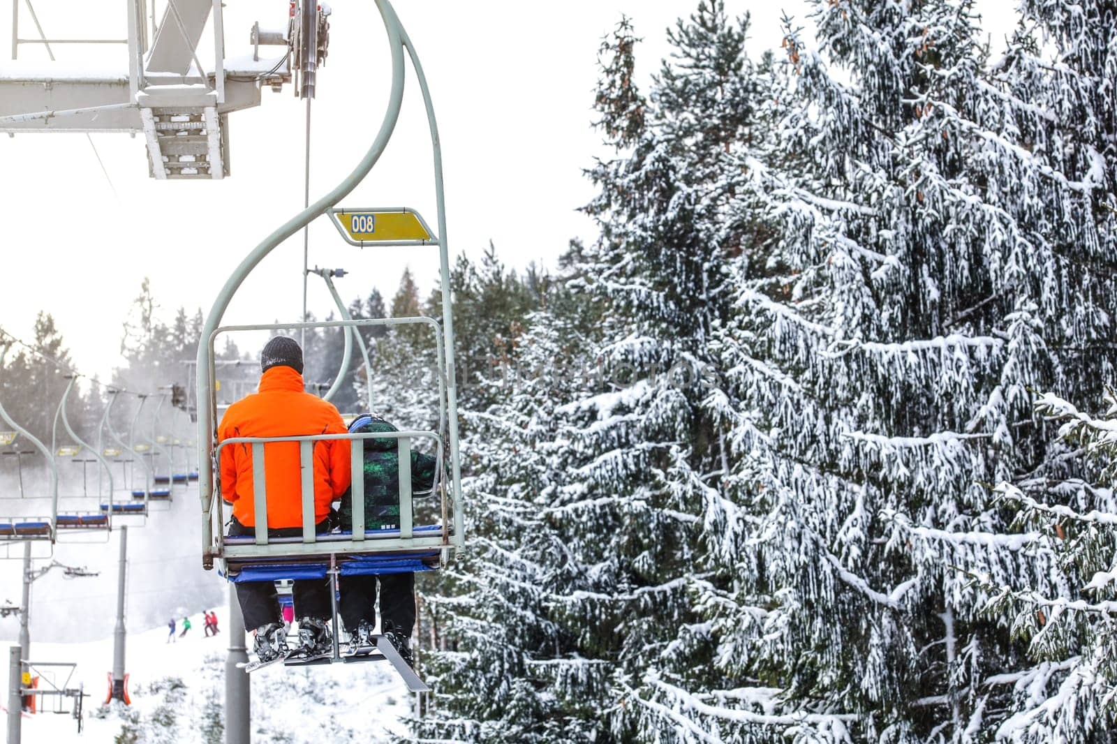 Skiers on chair lift, piste under, snow covered trees on right side by Ivanko