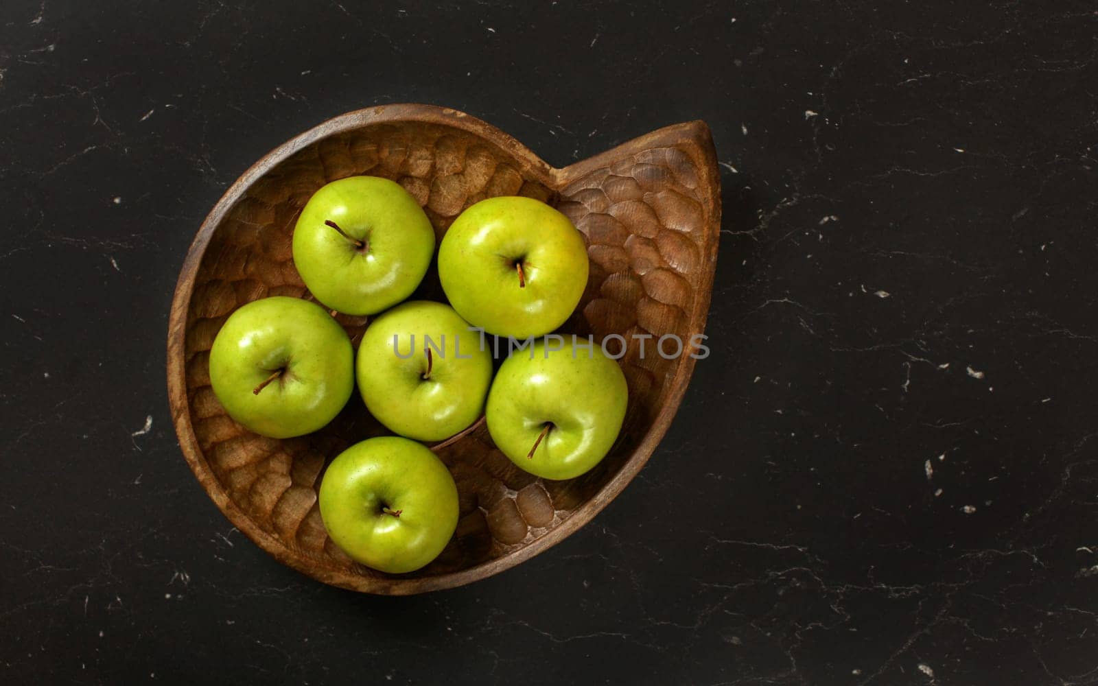 Top down view, six green apples in wooden carved bowl, on black marble like board. by Ivanko