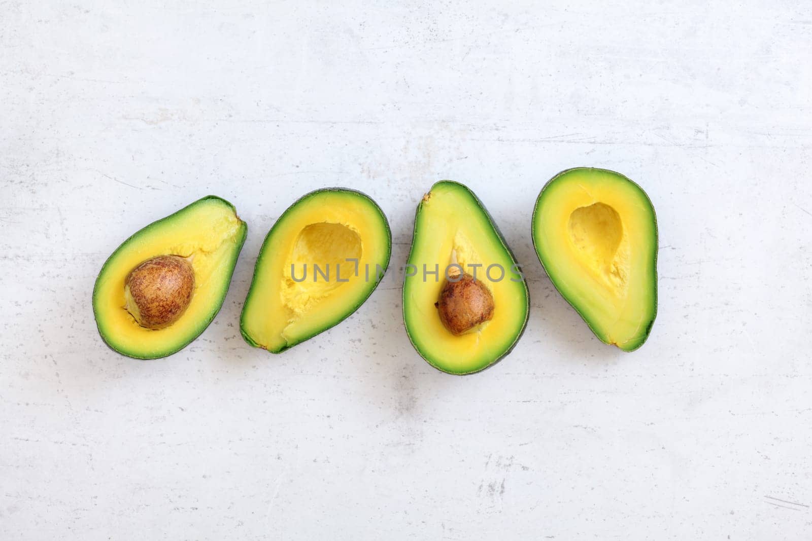 Top down view, two avocados cut in half, halves with seed visible , on white stone like board. Space for text above, and below.