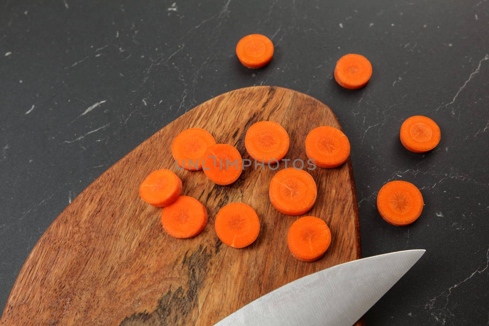 Top down view, carrot sliced to circles, chopping desk, blade of chef knife next on black marble like working board by Ivanko